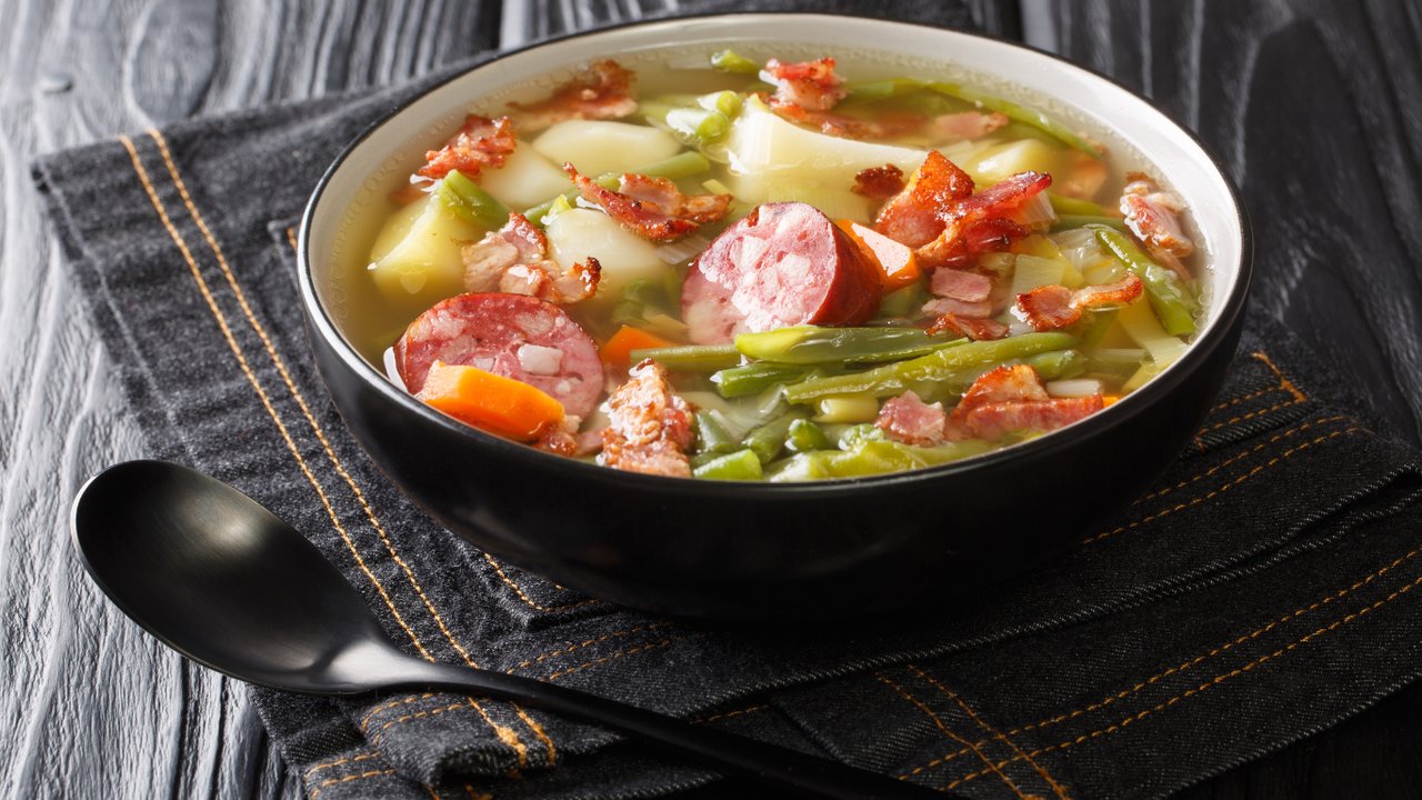 Luxembourgish bean soup (Bouneschlupp) with bacon, potato, sausages and onions on a table