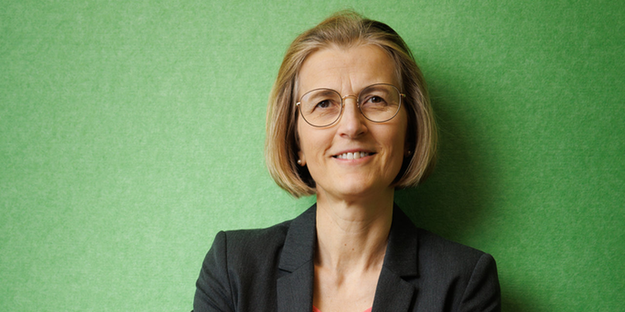 Photo of Monika Henzinger standing in front of green wall